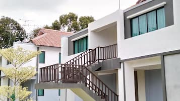 A modern residential building with a staircase leading to an upper floor, surrounded by greenery.
