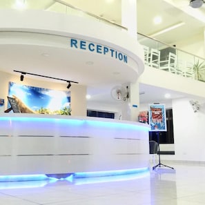 A reception desk with a sign that reads 'RECEPTION' and a digital screen displaying a scenic image. - Bayu Balau Beach Resort (Bandar Penawar)