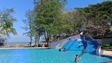 A swimming pool with a water slide and a beach view.