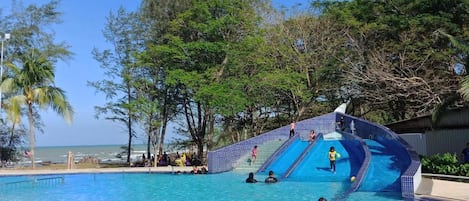 A swimming pool with a water slide and a beach view.