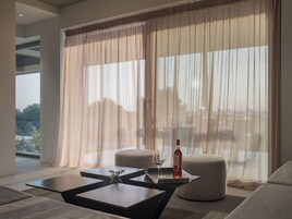 Un salón moderno con un amplio ventanal, una mesa de centro de vidrio y dos otomanas.