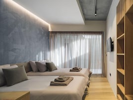 Un dormitorio moderno con dos camas, un ventanal con cortinas translúcidas y un armario de madera.