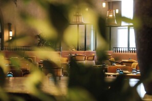 A restaurant interior with seating arrangements, pendant lighting, and a view through a window. - W Riyadh Kafd (Riyadh)