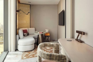 A modern hotel room with a sofa, a small round table, a chair, a TV mounted on the wall, and a view of the city. - W Riyadh Kafd (Riyadh)