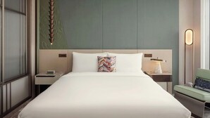 Quarto de hotel com uma cama grande, mesa de cabeceira, luminária e uma cadeira.