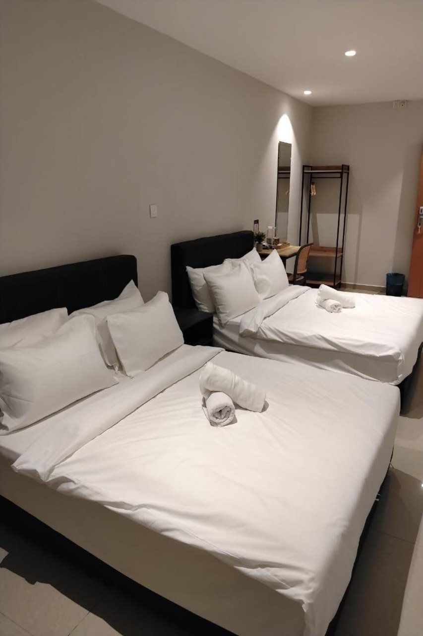 A hotel room with two beds, a nightstand, a mirror, and a small table with a lamp.