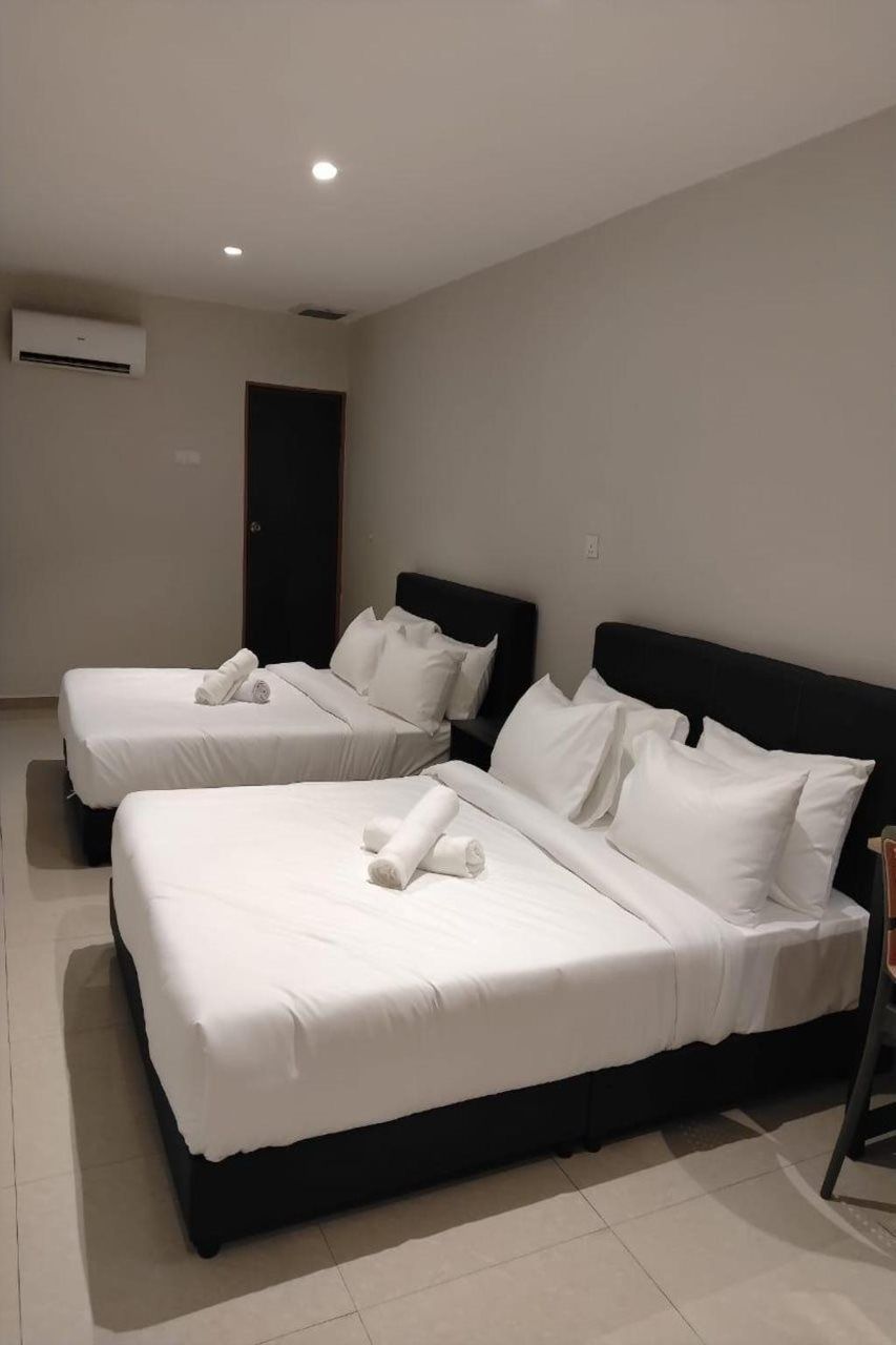 A hotel room with two beds, each with white linens and pillows, a dark headboard, and an air conditioning unit on the wall.