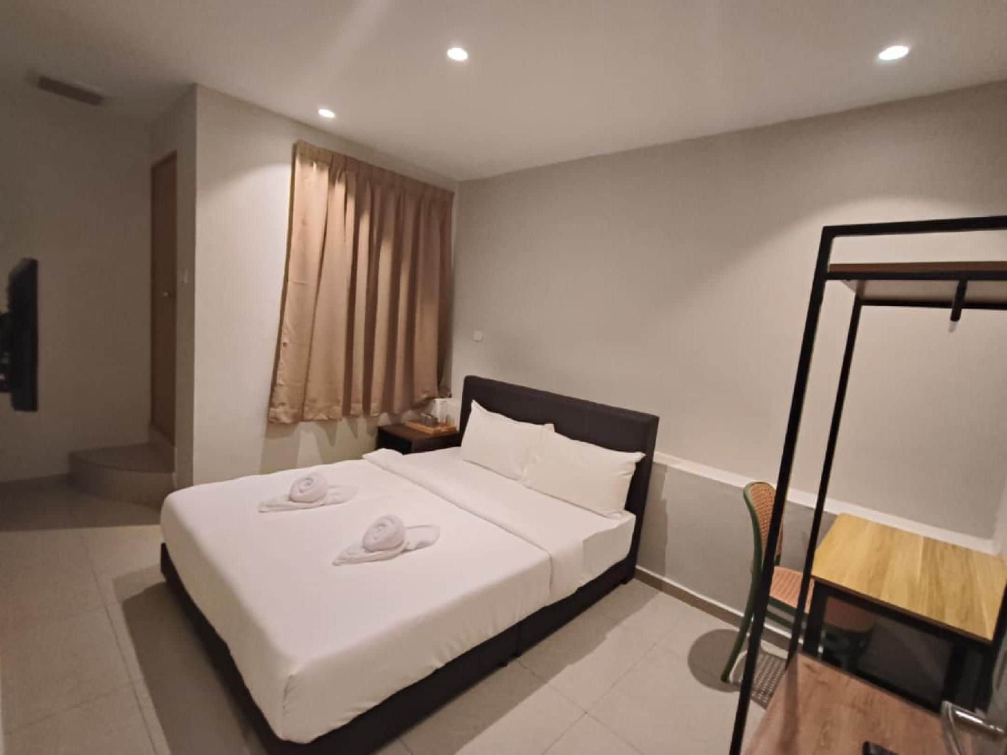 A hotel room with a bed, a wooden side table, a chair, and a window with curtains.