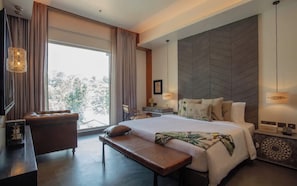 Una habitación de hotel moderna con una cama grande, un banco, un escritorio y vistas al exterior.