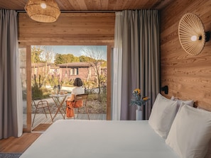 Une chambre avec un grand lit, des murs en bois, une vue sur un jardin et un coin repas avec une table et des chaises.
