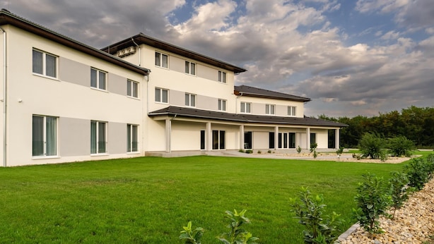 A multi-story residential building with a flat roof, large windows, and a well-maintained lawn. - NOA Hotel (Vecsés)