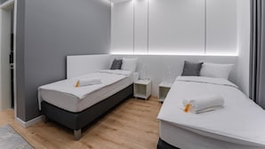 A modern hotel room with two single beds, a bedside table with a lamp, and a built-in wardrobe. - NOA Hotel (Vecsés)