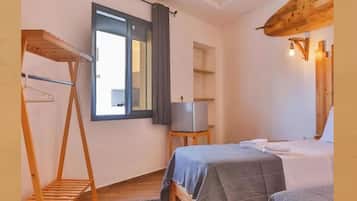 A room with two beds, a wooden shelf, a small table, a mirror, and a window with curtains.