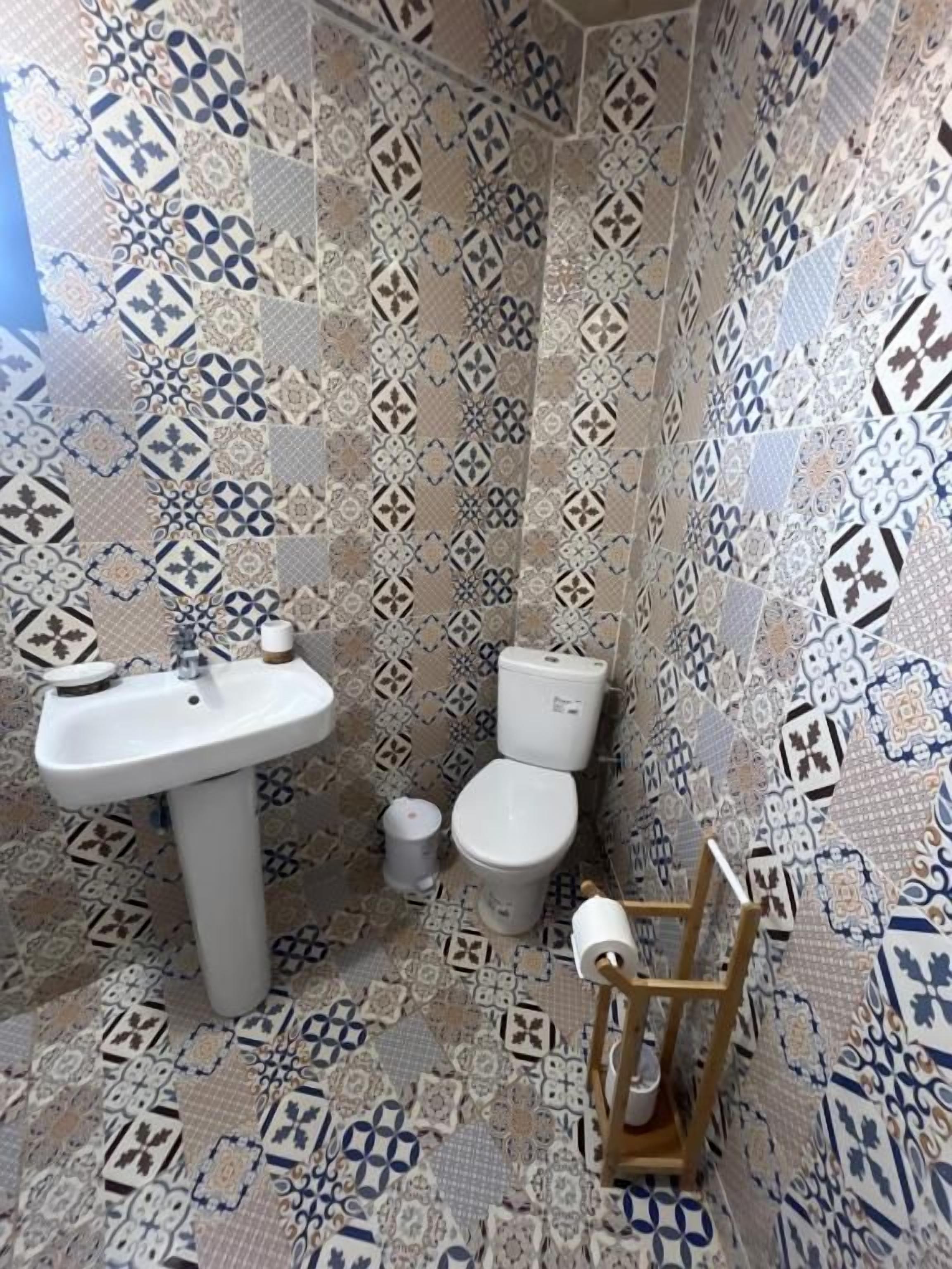 Een badkamer met patroon betegelde vloertegels, een wastafel, toilet en een houten stoel.