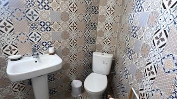 Een badkamer met patroon betegelde vloertegels, een wastafel, toilet en een houten stoel.