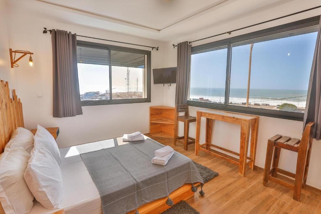 A bedroom with a bed, a desk, a TV, and large windows with a view of the sea.