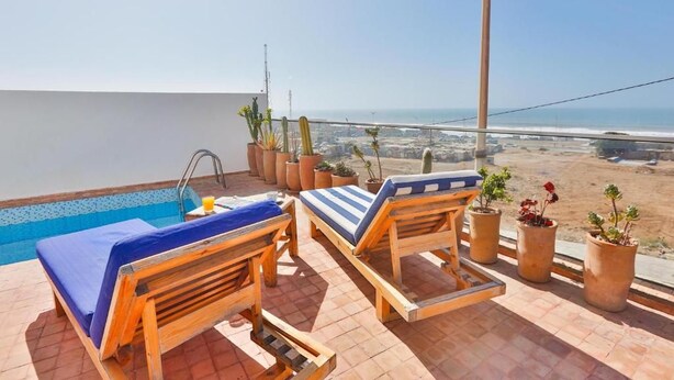 A rooftop pool area with two wooden lounge chairs, a small pool, and potted plants. - Moon surf (Imsouane mroc)