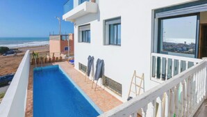 A modern building with a swimming pool, a balcony with a view of the beach, and a large window.
