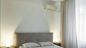 Un dormitori amb un llit, sivelles, aire condicionat i una finestra amb cortines.