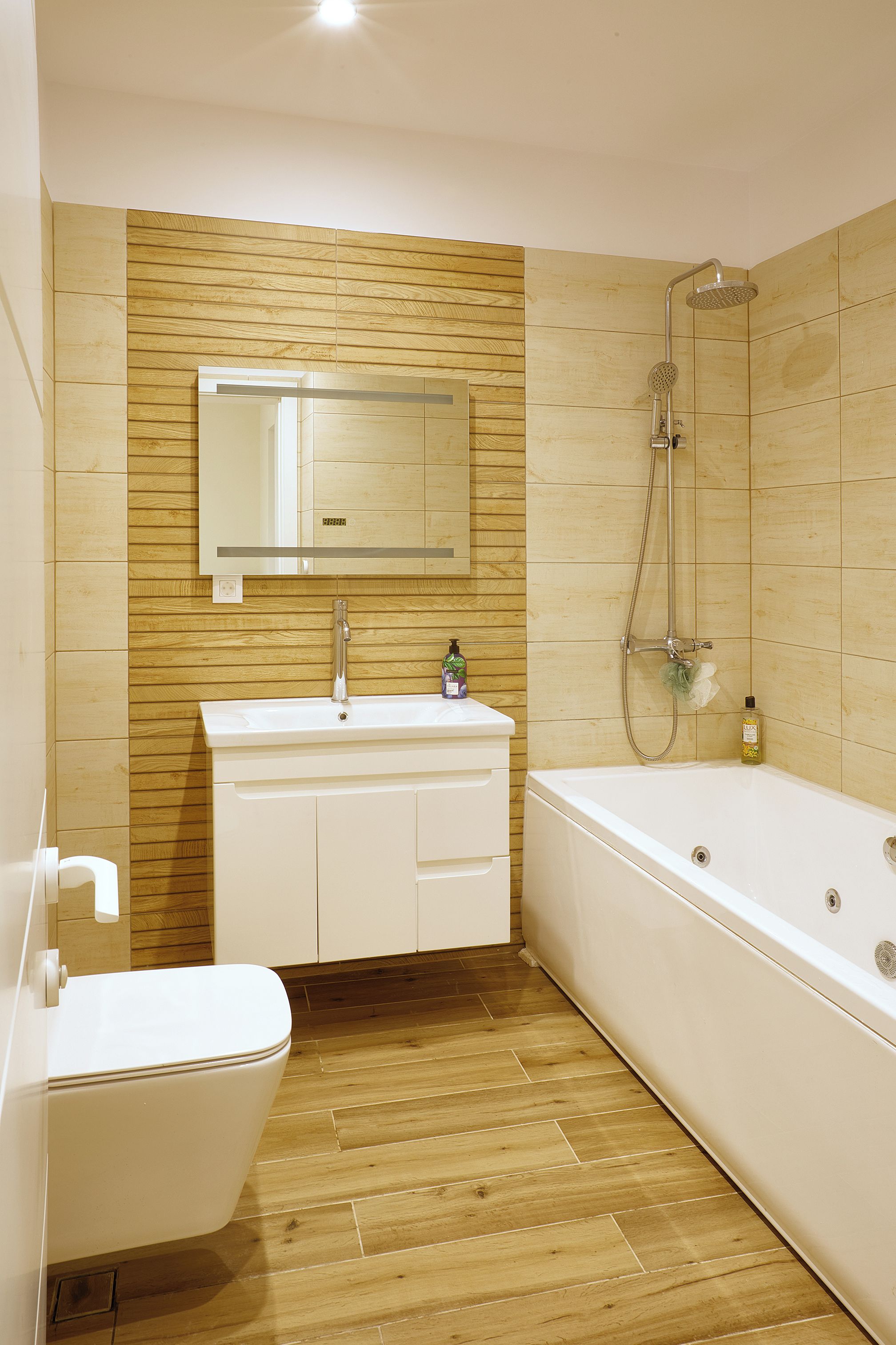 Ein Badezimmer mit Holzwand, Waschbecken in Weiß, Spiegel, Dusche und Toilette.