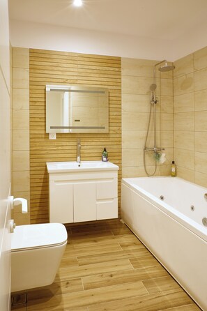 Ein Badezimmer mit Holzwand, Waschbecken in Weiß, Spiegel, Dusche und Toilette.