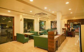 A restaurant with green upholstered booths, a wooden counter, and a tiled floor. - Hotel Dwarka Park (Rahata)