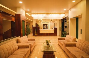 A hotel lobby with a reception desk, two sofas, a chandelier, and a potted plant on a glass table. - Hotel Dwarka Park (Rahata)