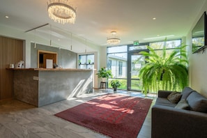 A reception area with a reception desk, a red rug, a sofa, and a large plant.