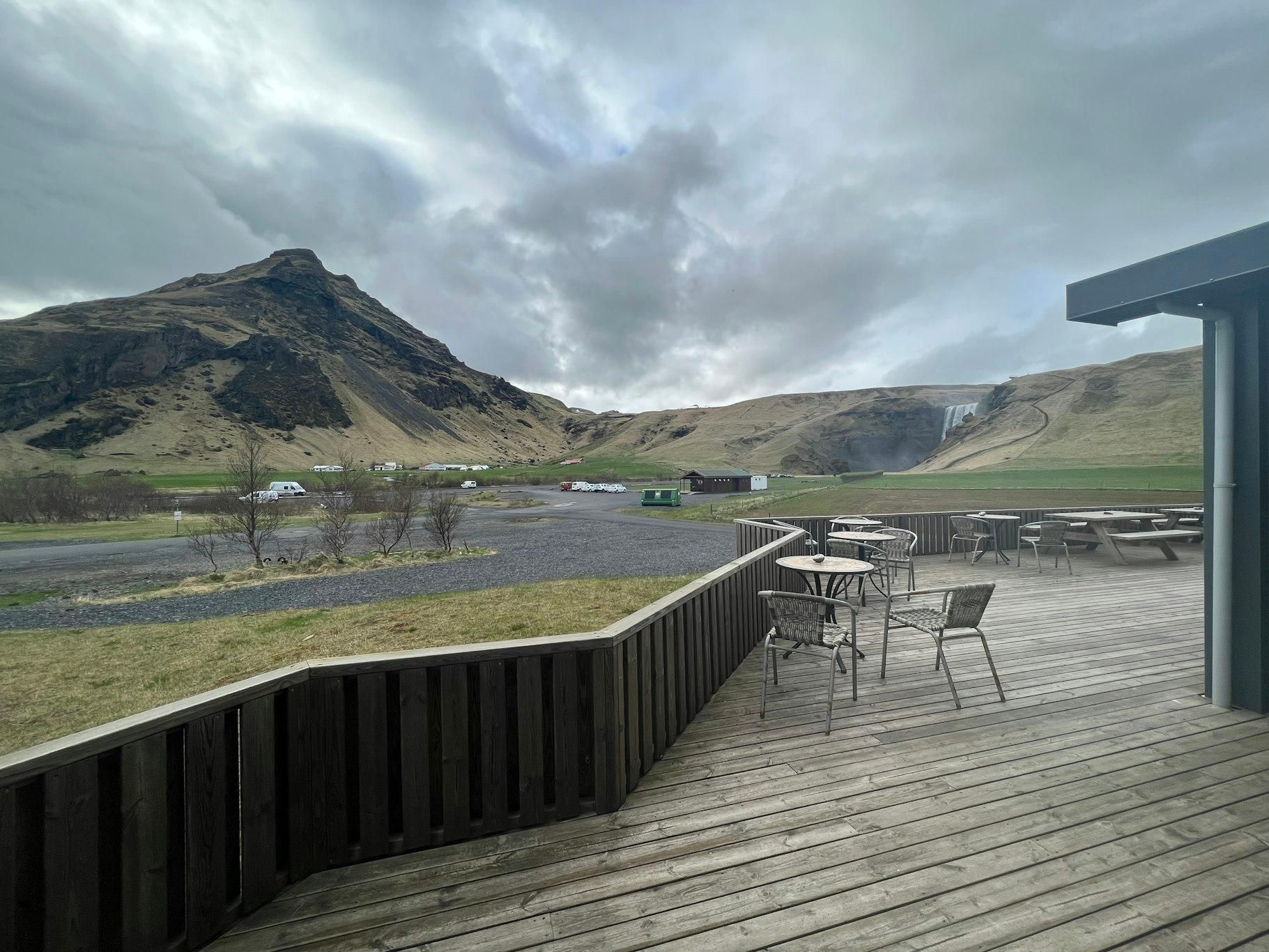 A wooden deck with outdoor seating, overlooking a mountainous landscape with a waterfall.