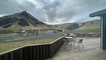 A wooden deck with outdoor seating, overlooking a mountainous landscape with a waterfall.