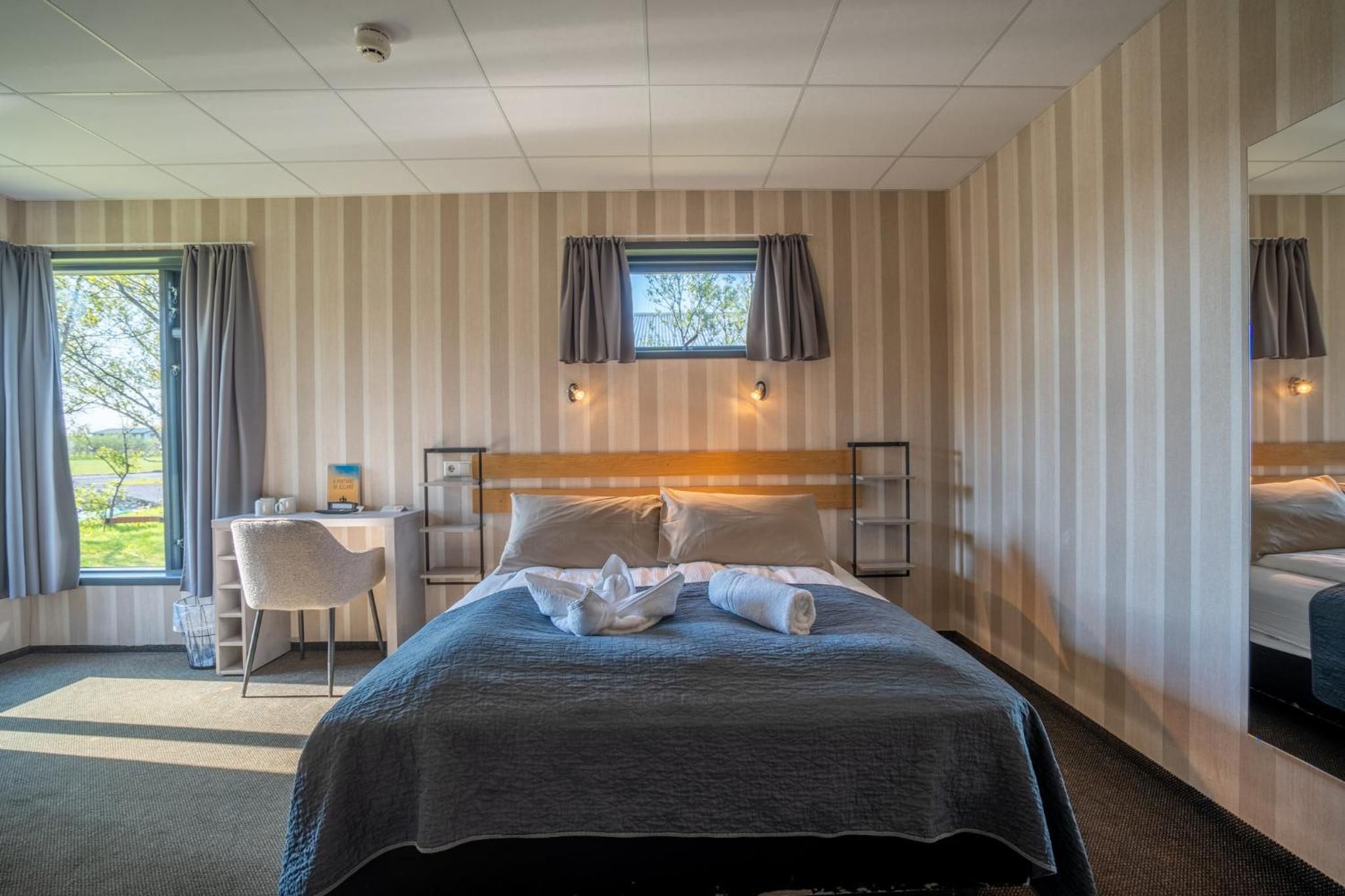 A hotel room with a bed, a desk, a chair, a window with curtains, and a view of the outdoors.