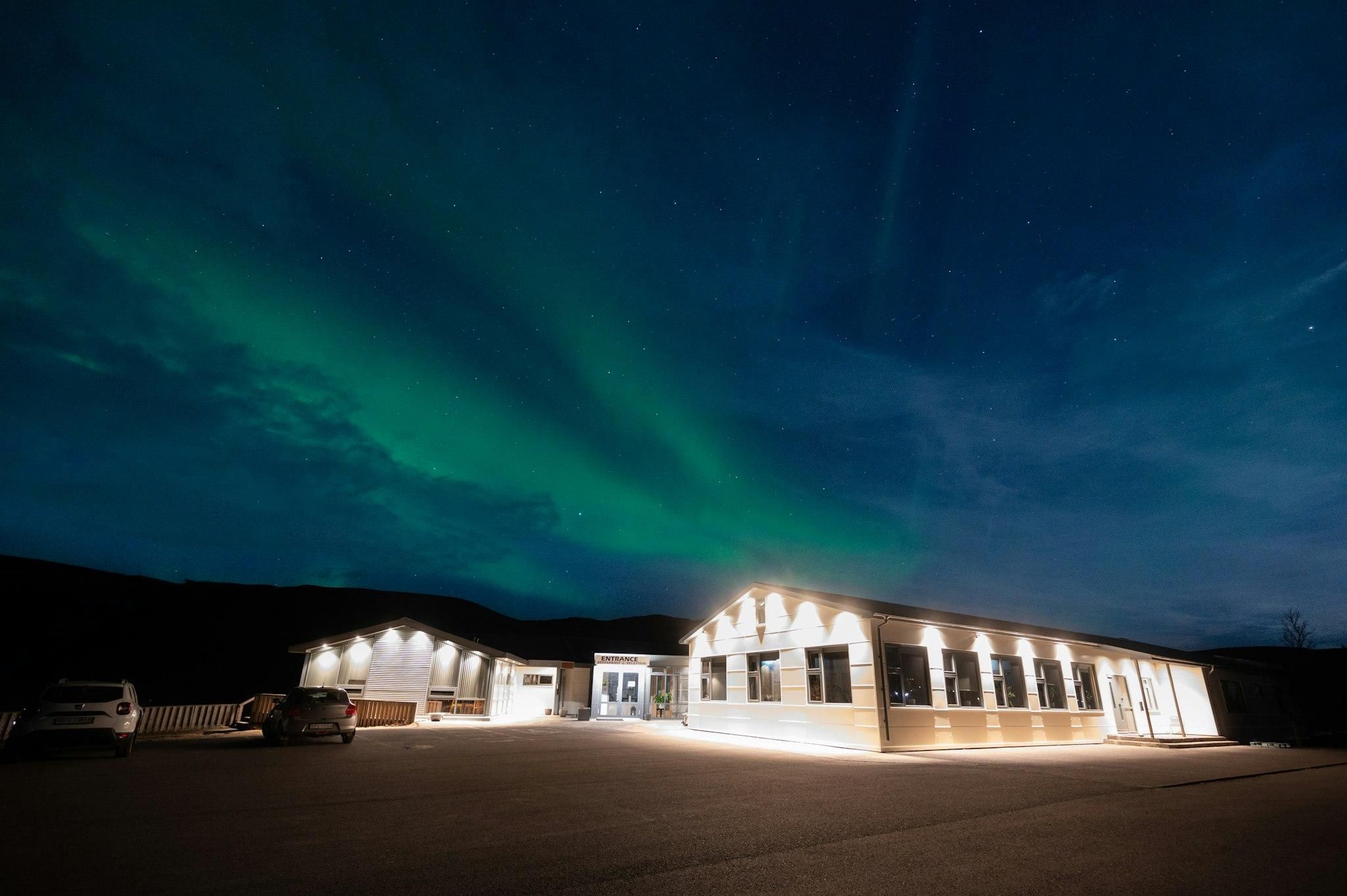 A building with an entrance sign, parking area, and a view of the night sky with aurora borealis.