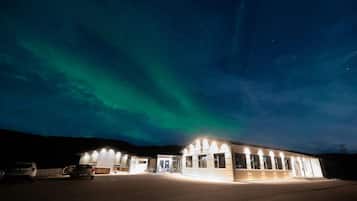 A building with an entrance sign, parking area, and a view of the night sky with aurora borealis.