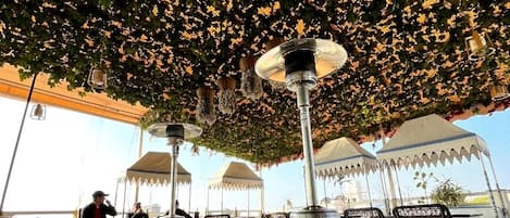 An outdoor seating area with patterned floor tiles, a central column, and a decorative ceiling.