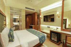A hotel room with a bed, a television, a desk, and a mirror. - Shera Hotels & Banquets (Navi Mumbai)