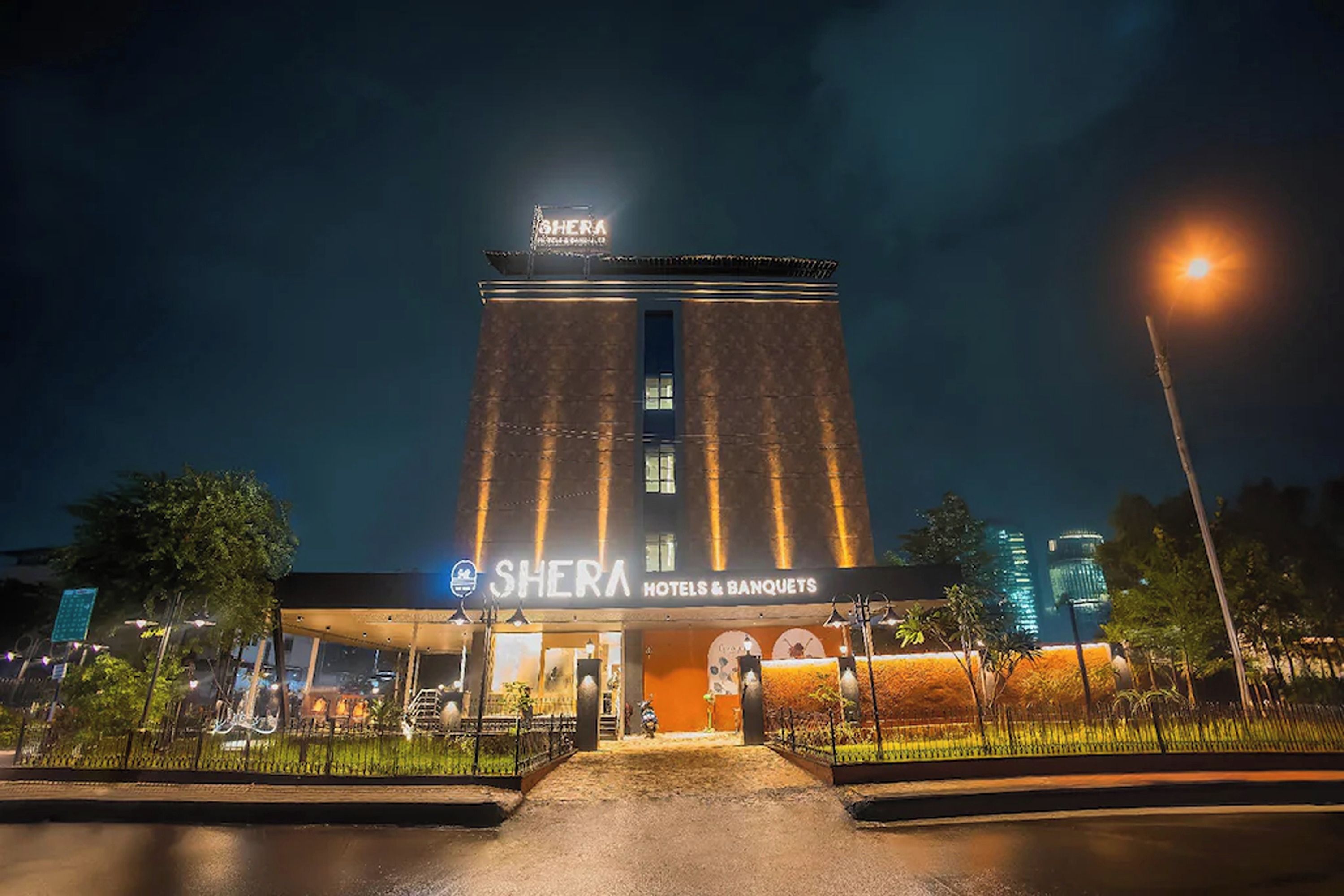 A hotel named 'SHERA' with a modern design, featuring a prominent entrance and a well-lit facade.