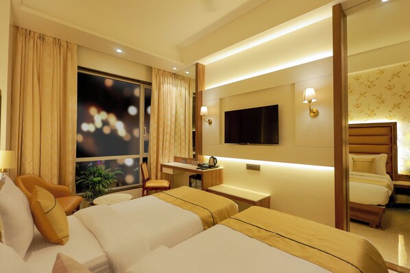 Una habitación de hotel con dos camas, un escritorio, una silla, un televisor y una ventana con cortinas.