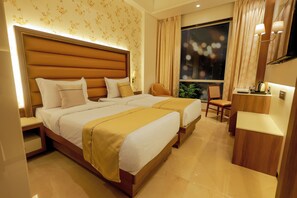 Habitación de hotel con dos camas, un escritorio, una silla y un ventanal con cortinas.