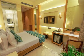 Una habitación de hotel moderna con una cama grande, un escritorio con televisor, un espejo y un refrigerador pequeño.