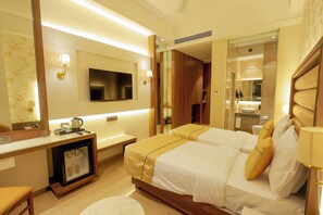 Habitación de hotel con dos camas, un escritorio con refrigerador, televisor y espejo.