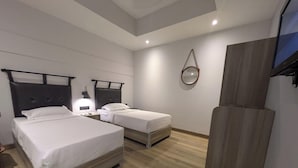 Una habitación de hotel con dos camas, piso de madera, un espejo y un televisor.