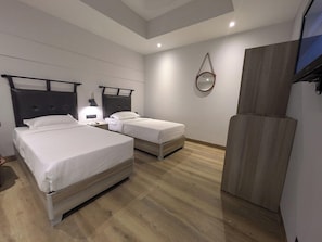 Une chambre d’hôtel avec deux lits, un plancher en bois, un miroir et une télévision.