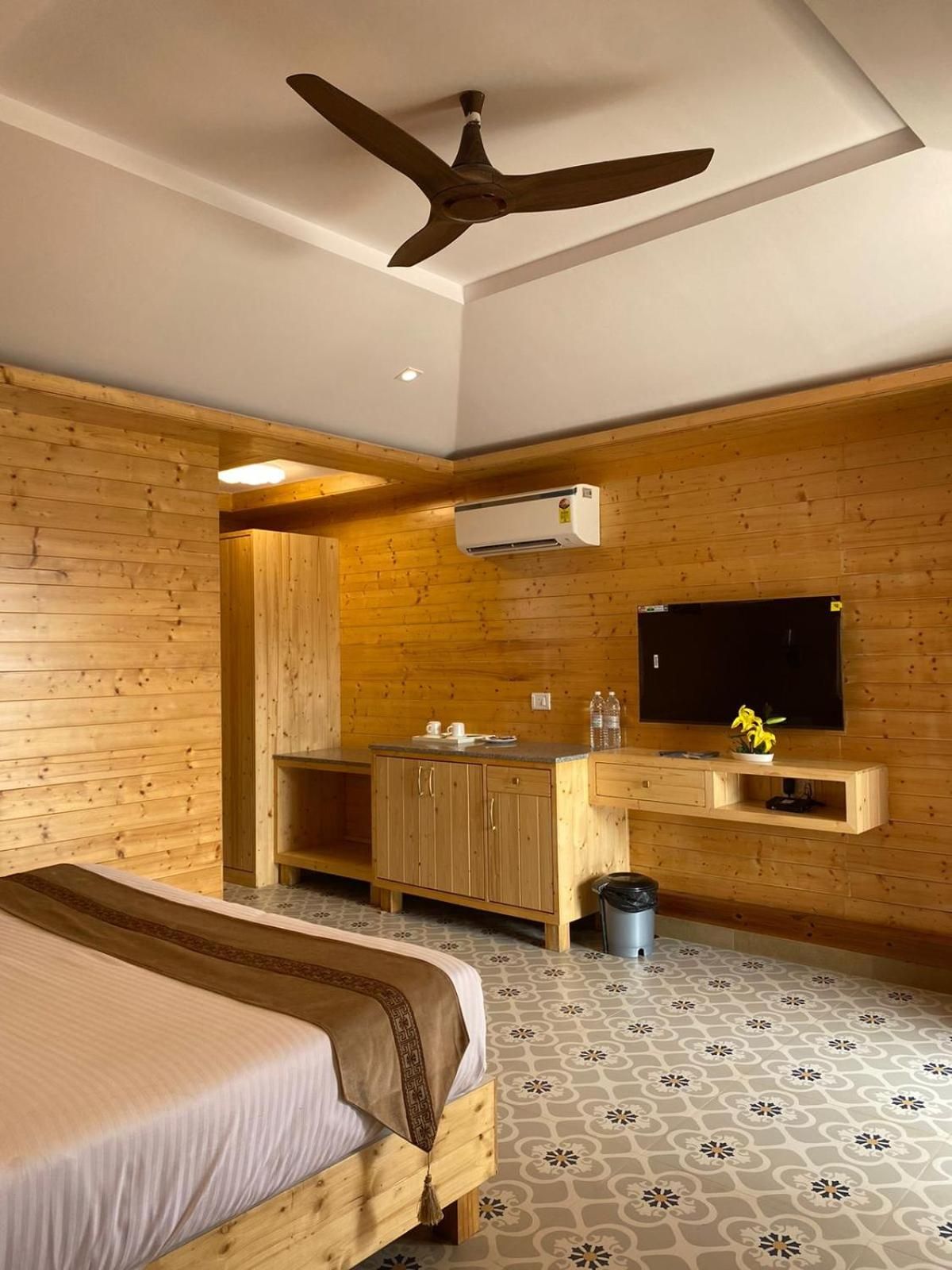 Une chambre avec un lit, une armoire en bois, un téléviseur et un ventilateur de plafond.