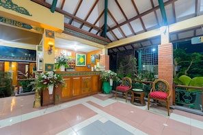 Un área de recepción con mostrador de madera, sillas y plantas en macetas.