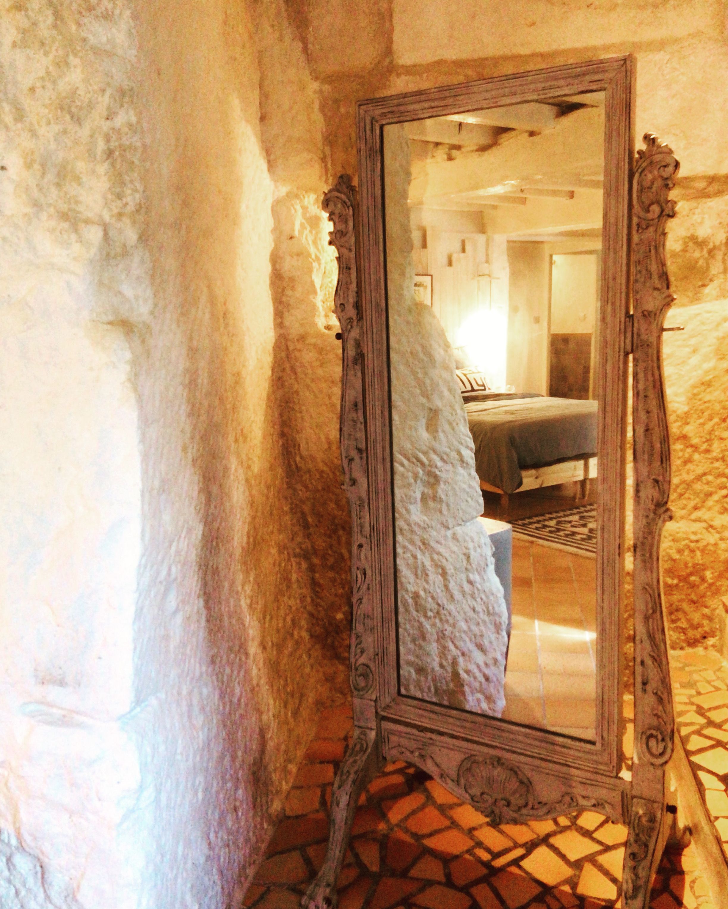 A mirror with an ornate frame reflecting a bedroom with a bed and a door.