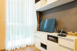 A modern living room with a flat-screen TV, a bookshelf, and a window with sheer curtains. - Resort Style Condo - Heart of Bangkok (Bangkok)