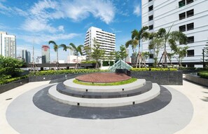 A circular plaza with a central wooden deck, surrounded by a low wall with greenery and palm trees. - Resort Style Condo - Heart of Bangkok (Bangkok)