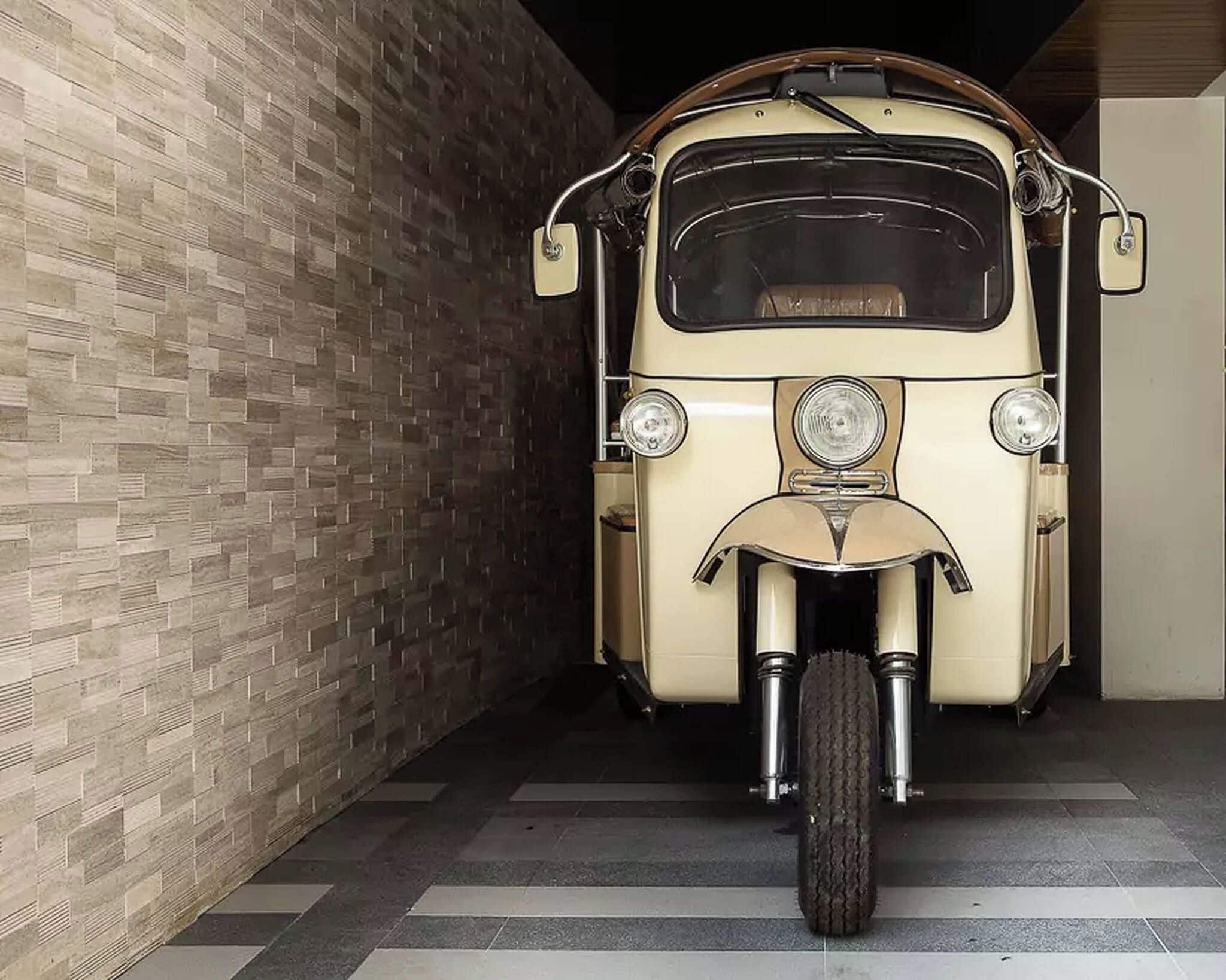 A vintage car parked in a garage with a tiled floor and a brick wall.