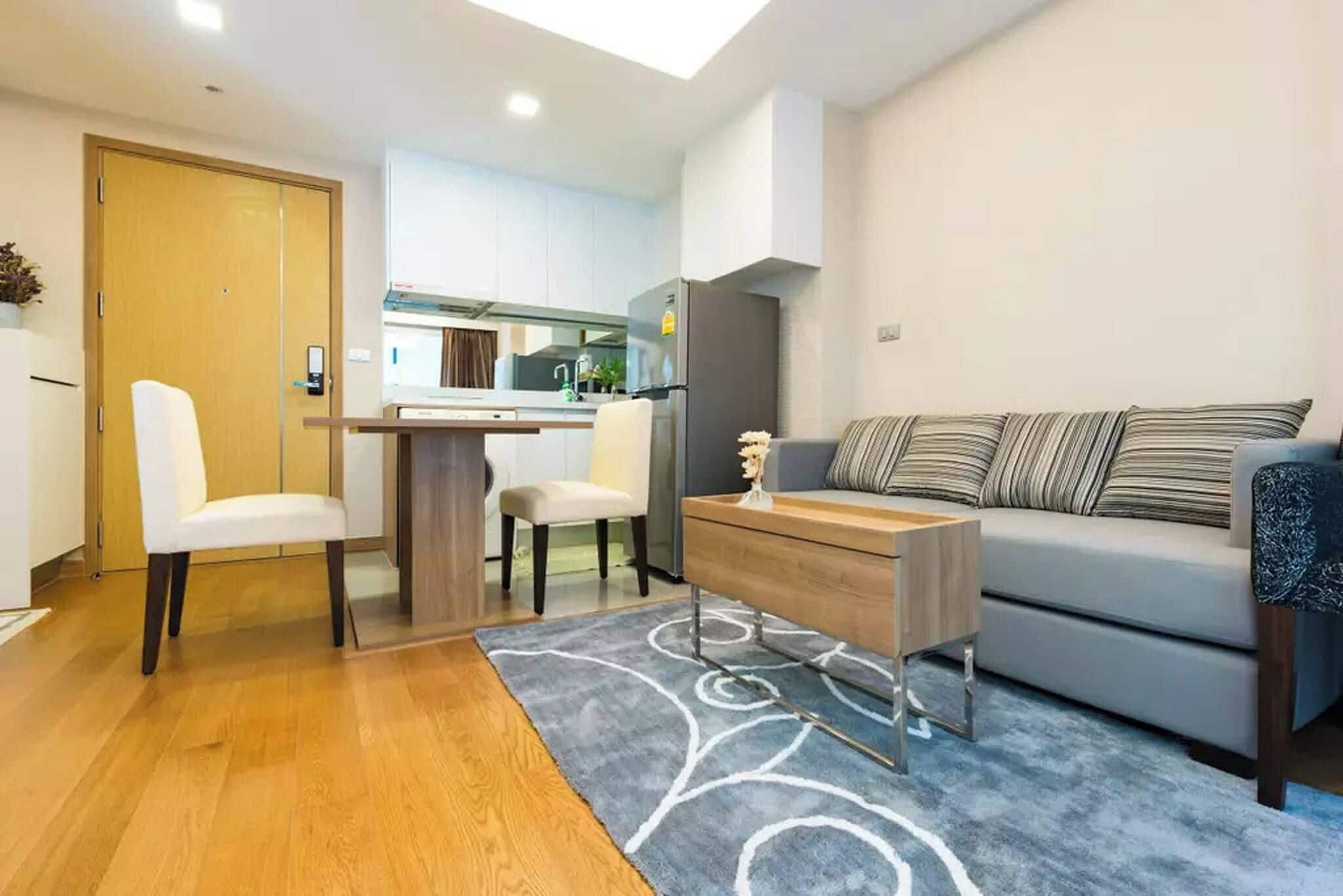 A modern living room with a sofa, two chairs, a coffee table, and a kitchen area in the background.