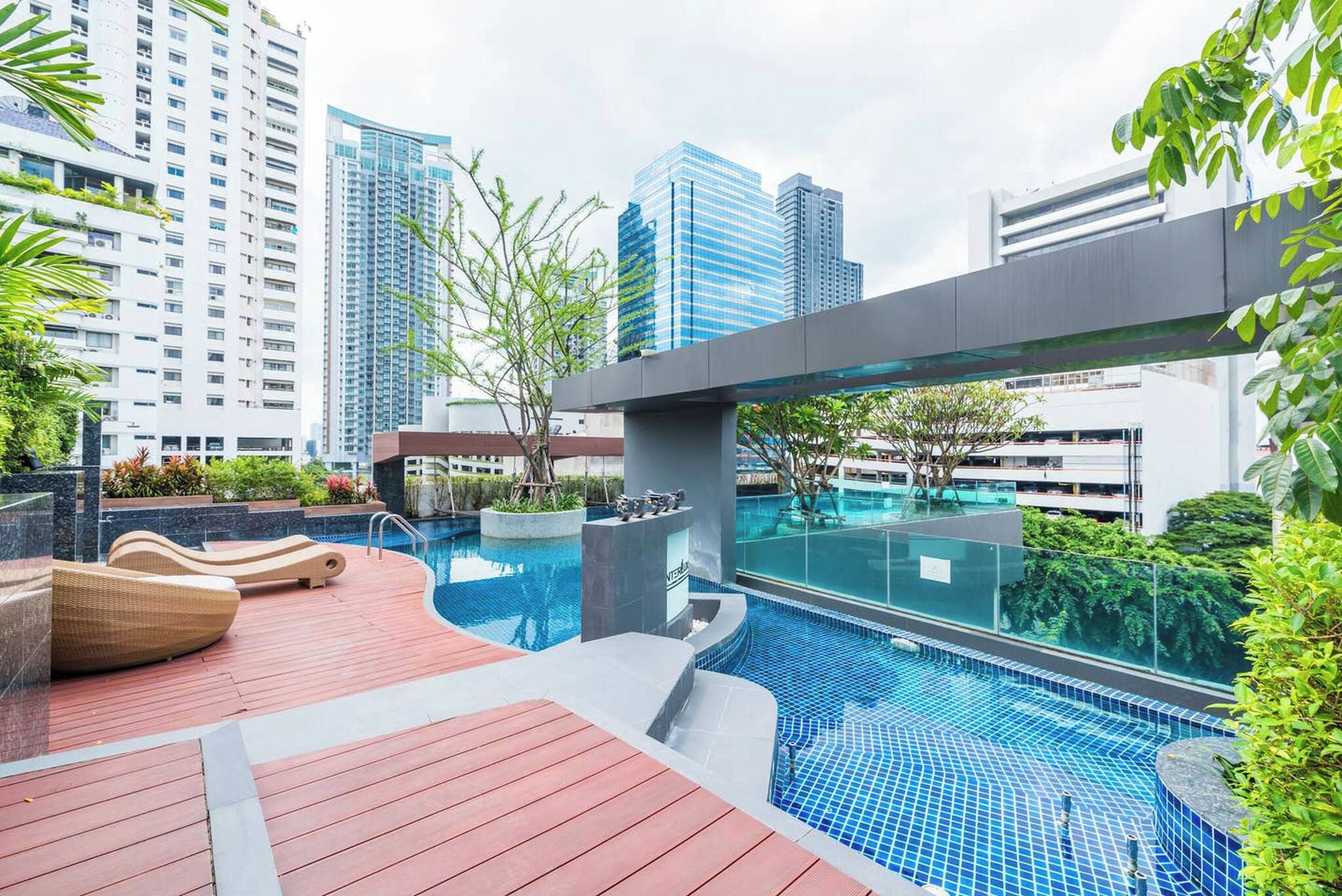 A rooftop swimming pool with lounge chairs, surrounded by greenery and modern buildings.